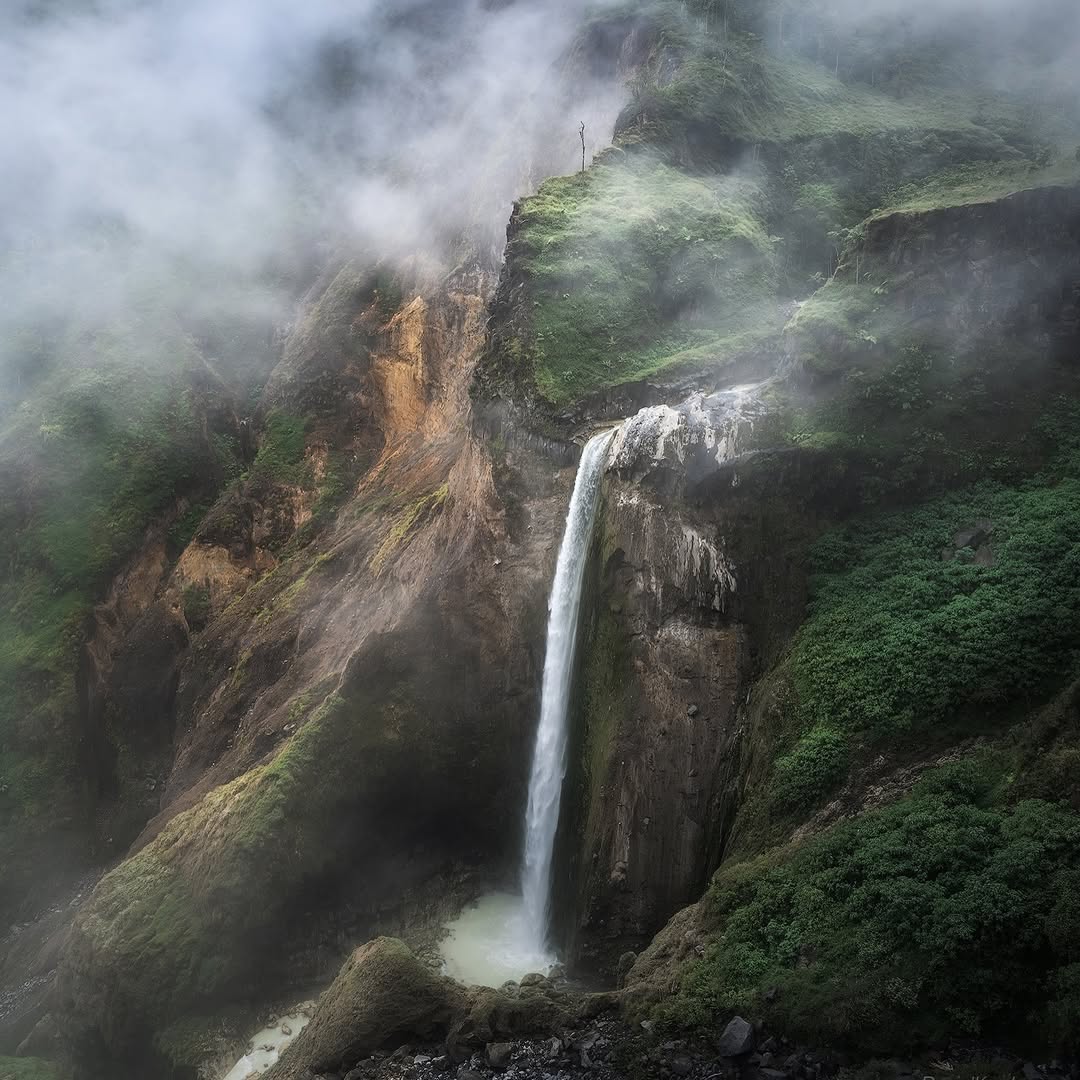 Penimbungan Waterfall cascading down a towering cliff on the slopes of Mount Rinjani, surrounded by lush tropical forest in Lombok, Indonesia.